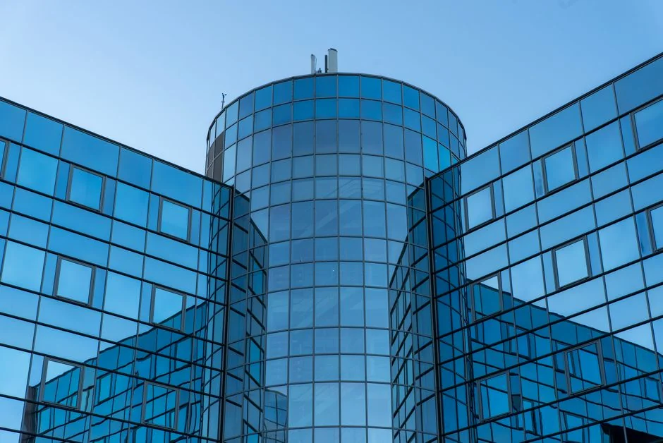 our-story Two workers cleaning windows on a glass building facade using a lift platform, enhancing building aesthetics.