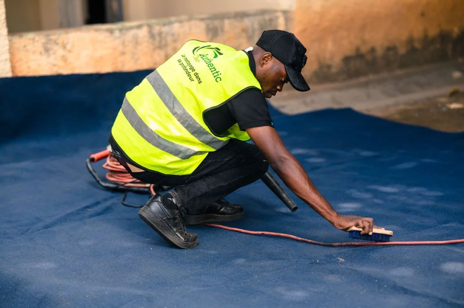 A man cleaning a glass barrier outdoors with a squeegee, surrounded by greenery.